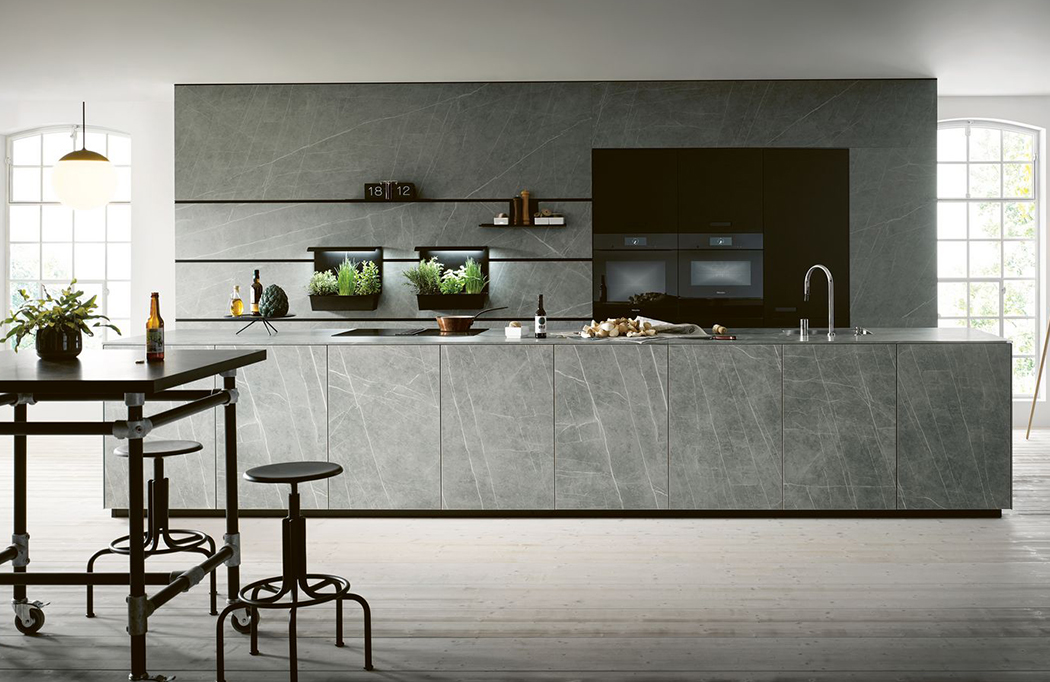 Große Küchenzeile mit Insel in Marmor-Optik. Auf der Kücheninsel befinden sich Waschbecken und Kochfeld. An der Küchenzeile ist das Wandorganisationssystem next125 Cube montiert.