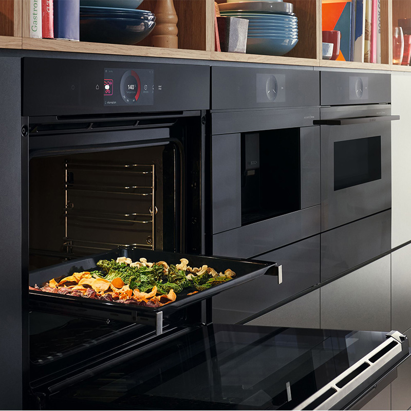 Drei Küchengeräte von Bosch, der Backofen ist geöffnet und auf einem Backblech befinden sich verschiedene Gemüsesorten.